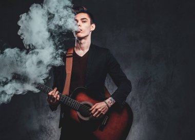 Çekici adam akustik gitar çalıyor ve sigara içiyor
