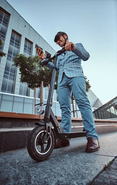 El hombre está conduciendo su nuevo scooter eléctrico cerca de un gran edificio de vidrio —  Fotos de Stock