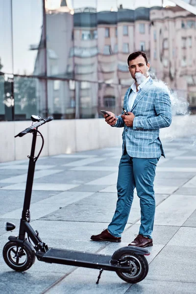 Elegante hombre con electro scooter está fumando vapor —  Fotos de Stock