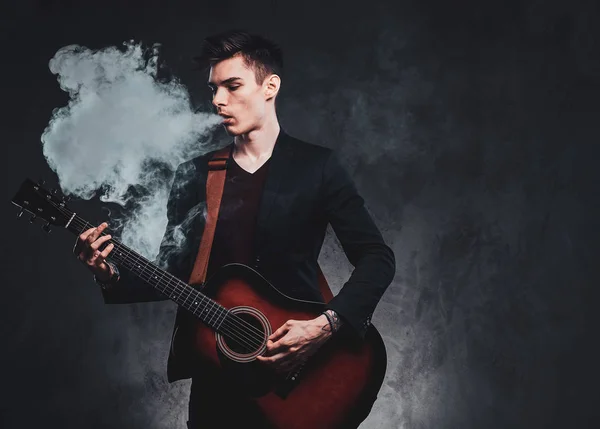 El chico atractivo está tocando la guitarra acústica y fumando — Foto de Stock