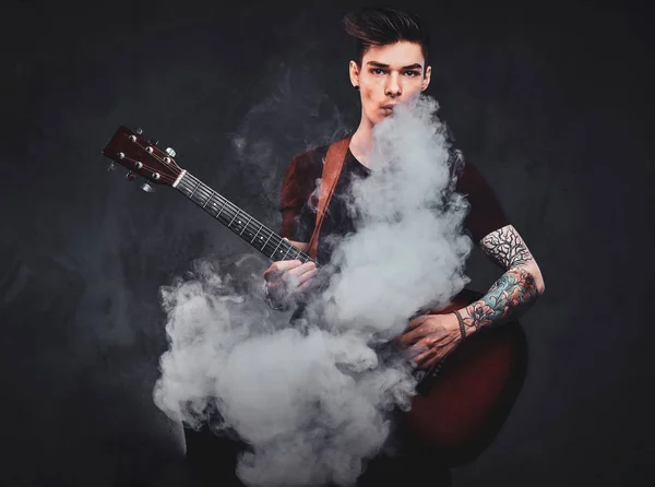El chico atractivo está tocando la guitarra acústica y fumando — Foto de Stock
