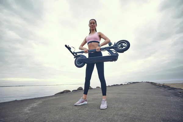 Mujer en ropa deportiva está sosteniendo plegado electro scooter —  Fotos de Stock