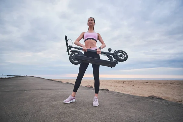 Mujer en ropa deportiva está sosteniendo plegado electro scooter —  Fotos de Stock