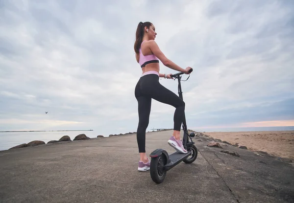 Sportieve vrouw rijdt Electro scooter aan zee — Stockfoto