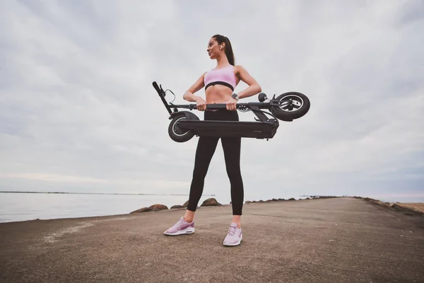 Mujer en ropa deportiva está sosteniendo plegado electro scooter —  Fotos de Stock