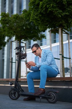 Yakışıklı erkek scooter ve akıllı telefon ile bankta rahatlatıcı