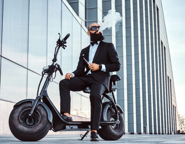 Elegante hombre de negocios está fumando mientras está sentado en bicicleta eléctrica —  Fotos de Stock