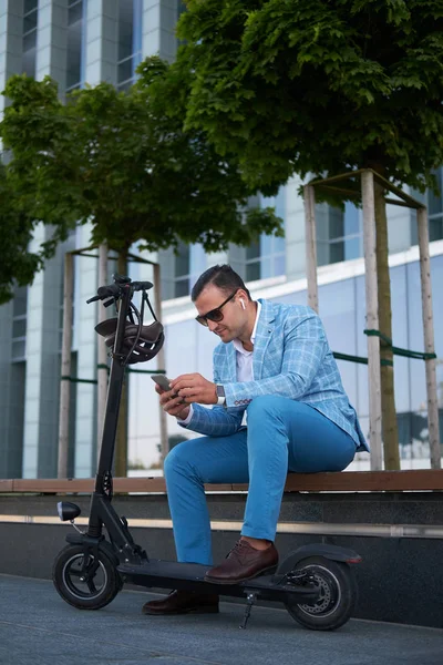 Jóképű férfi pihentető a padon, robogó és okostelefon — Stock Fotó