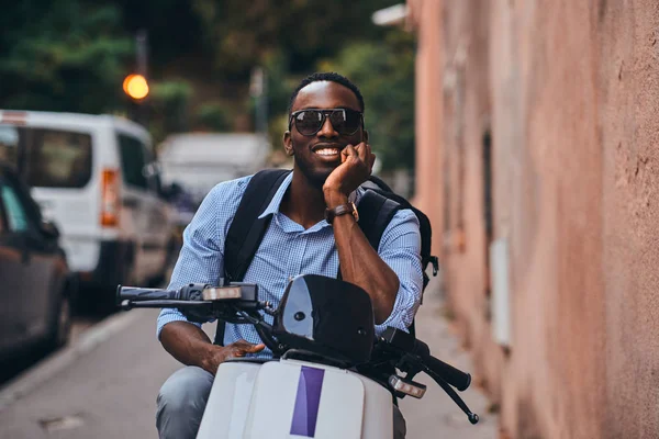 Young black man on scooter with mobile phone