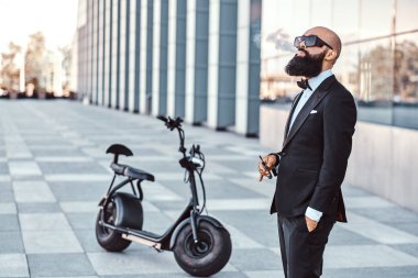 Zarif adam elektro bisikletinin yanında sigara içiyor.