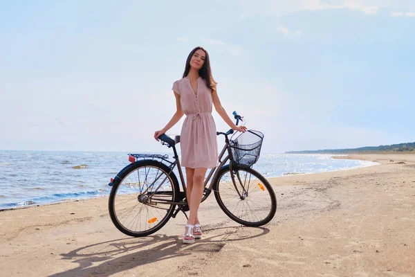 Portret van mooie brunette met haar fiets aan de kust — Stockfoto