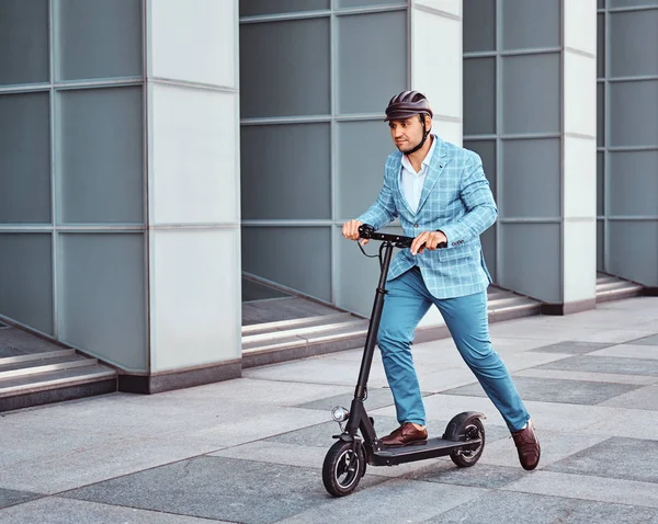 Bonito homem está montando sua scooter perto de escritórios edifício — Fotografia de Stock