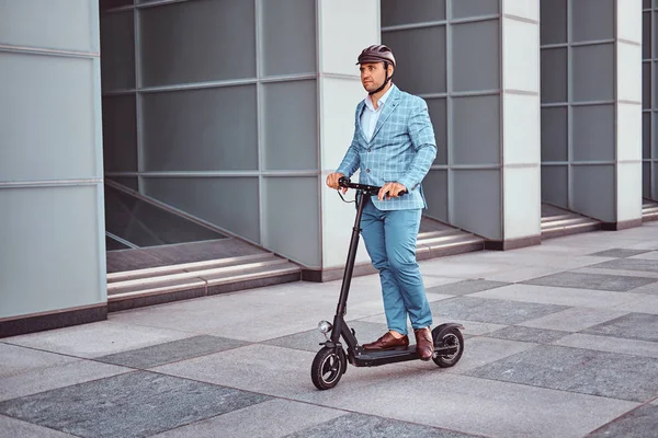 Bonito homem está montando sua scooter perto de escritórios edifício — Fotografia de Stock