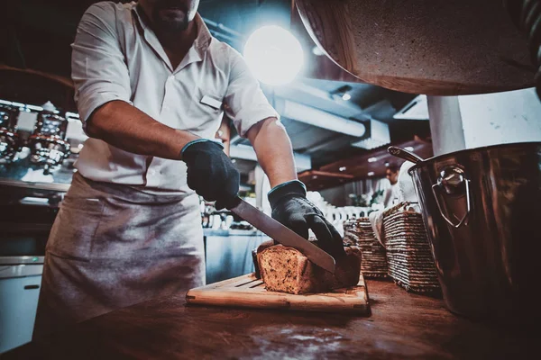 Kitchen worker is slicing bread for lunch — Stock Photo, Image