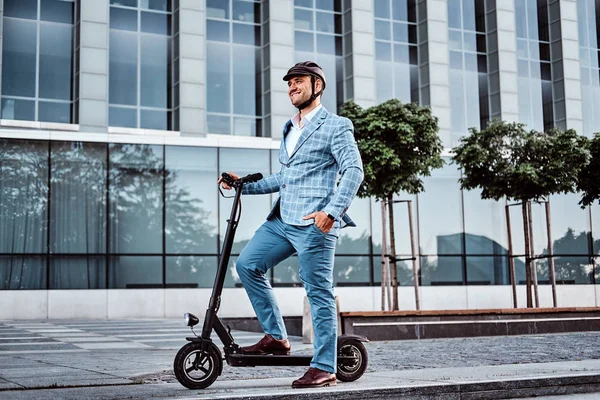 Bel homme est équitation son scooter près de bureaux bâtiment — Photo