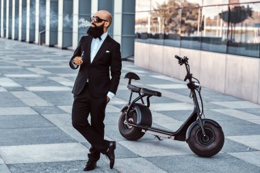 Zarif adam elektro bisikletinin yanında sigara içiyor.