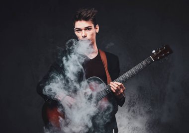 Çekici adam akustik gitar çalıyor ve sigara içiyor