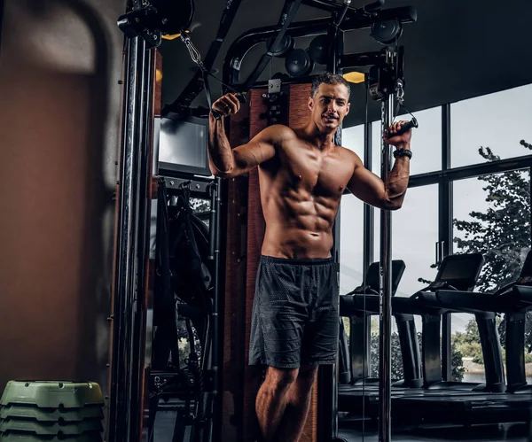 Muscular hombre está haciendo ejercicios con aparato de entrenamiento — Foto de Stock