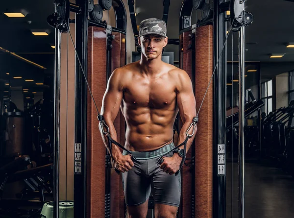 Homem muscular está fazendo exercícios com aparelho de treinamento — Fotografia de Stock