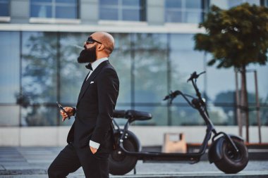 Zarif adam elektro bisikletinin yanında sigara içiyor.