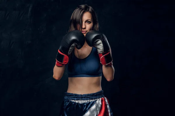 Mujer deportiva en ropa deportiva con casco protector y guantes de boxeo,  entrenando en el gimnasio. aislado sobre fondo oscuro con textura.