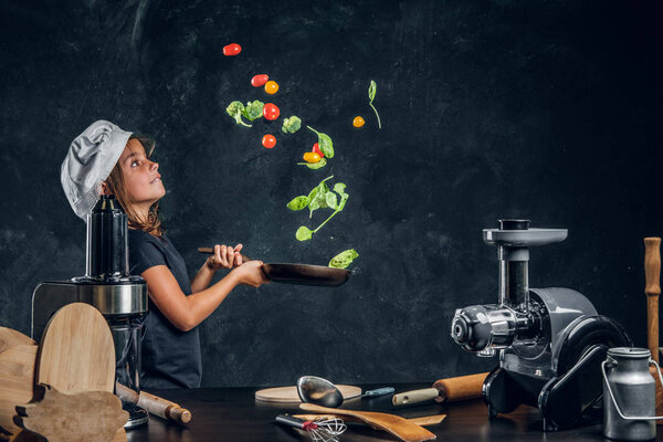 Little girl is tossing vegetables on the pan