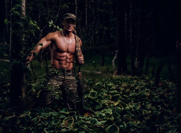 Jovem soldado bonito com tronco nu está andando na floresta profunda verde no dia quente de verão . — Fotografia de Stock