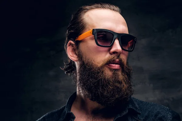 Bearded man in sunglasses is posing for photographer at dark photo studio. — Stock Photo, Image