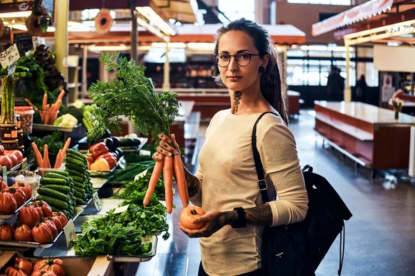 Jeune femme tatouée choisit des légumes de saison au marché — Photo