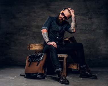 Dövmeli adam karanlık fotoğraf stüdyosunda oturuyor