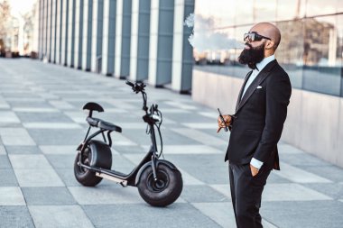 Zarif adam elektro bisikletinin yanında sigara içiyor.