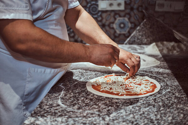 Experienced chef is adding cheese for his freshly made italian pizza.