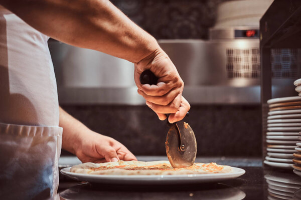 Chef is cutting tasty pizza with special knife at the kitchen.