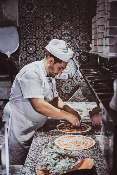 Experienced chef is adding decoration on freshly prepared pizza.