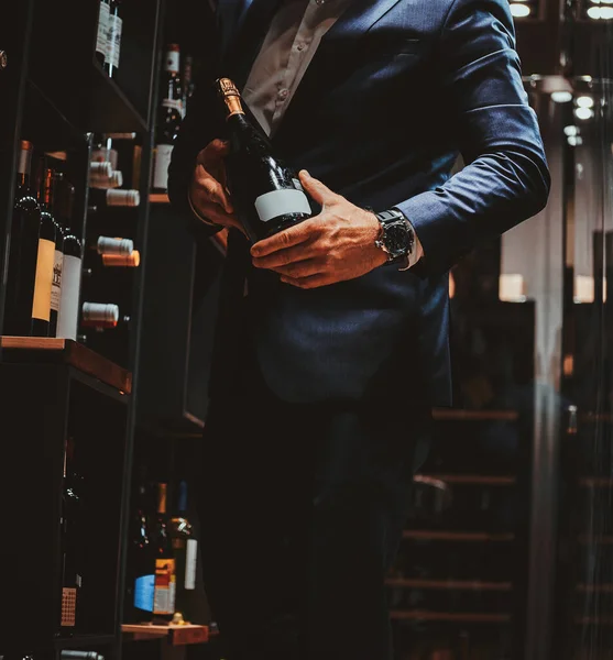 Элегантный мужчина в костюме в винном погребе с бутылкой вина — стоковое фото