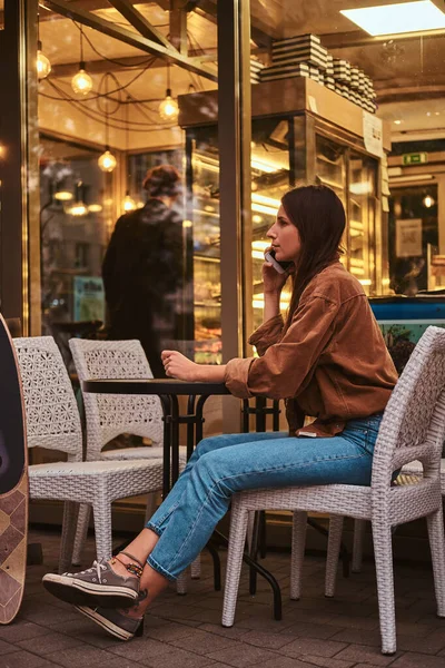 Morena está sentada no café com telefone celular — Fotografia de Stock