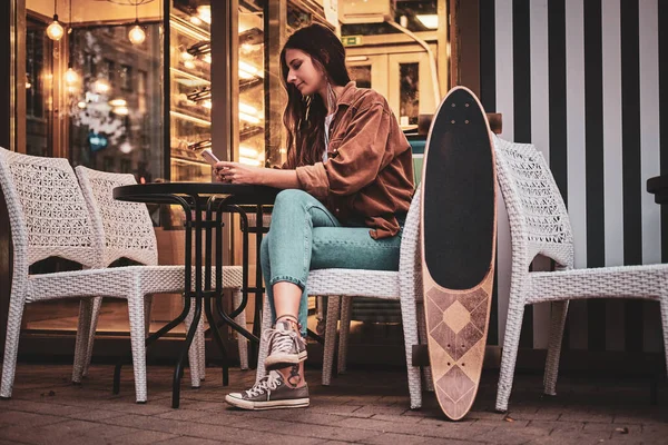 Dívka sedí v blízkosti kavárny s longboardem — Stock fotografie
