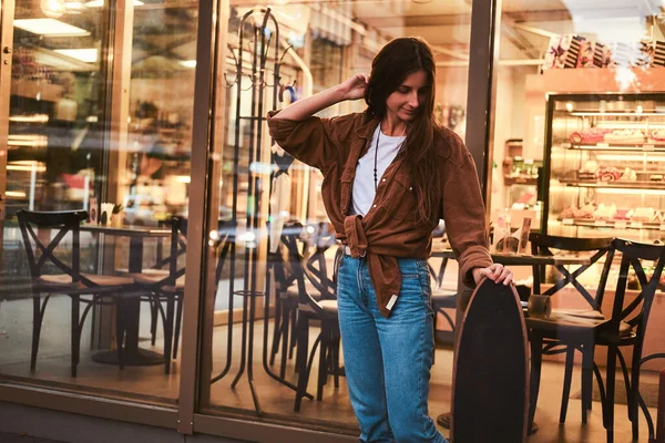 Chica está de pie cerca de café con longboard — Foto de Stock