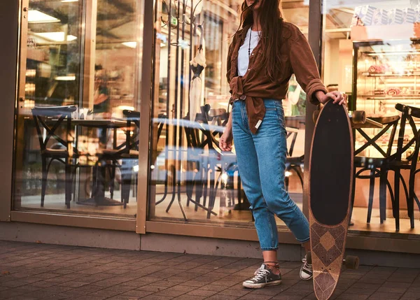 Meisje staat in de buurt cafe met longboard — Stockfoto