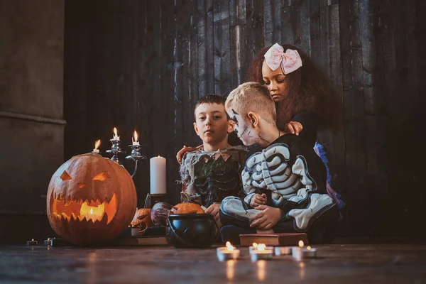 Niños bonitos en disfraces de Halloween están disfrutando de la fiesta mientras leen el libro . — Foto de Stock