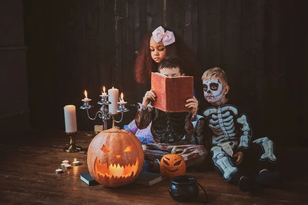Crianças bonitas em trajes de Halloween estão desfrutando de festa enquanto lêem o livro . — Fotografia de Stock
