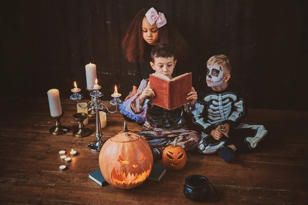 Crianças bonitas em trajes de Halloween estão desfrutando de festa enquanto lêem o livro . — Fotografia de Stock