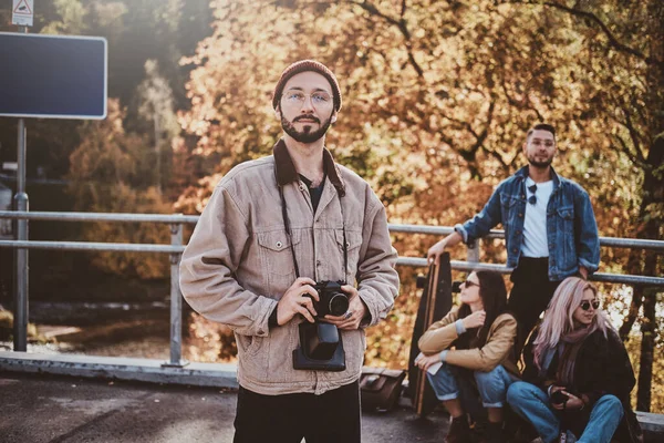 Young bearded hipster with camera and his friends — Stock Photo, Image