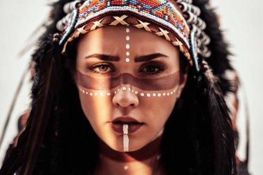 Aztek başlıklı, parlak bir stüdyoda poz veren cesur genç bir kadın.