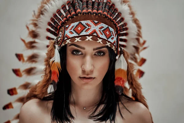 Magabiztos fiatal és meztelen nő pózol egy stúdióban törzsi fejdíszt viselve — Stock Fotó