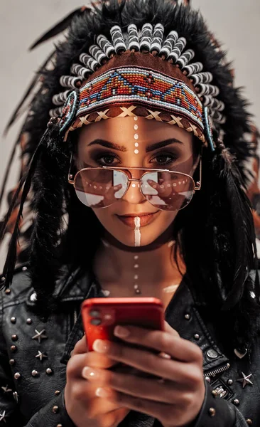 Attraktiv kvinna tittar på smartphone, bär tribal huvudbonad och orientalisk make-up — Stockfoto