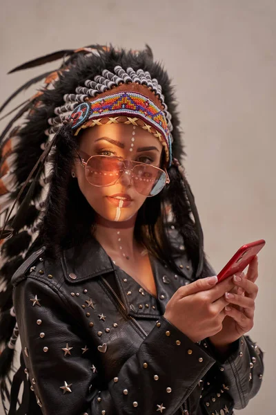 スマートフォンを見て魅力的な女性,部族の頭飾りと東洋の化粧を身に着けています — ストック写真