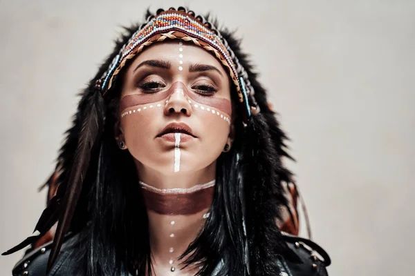 Calma modello femminile indossando copricapo capo azteco e trucco tribale in uno studio — Foto Stock