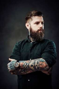 Koyu bir arka planda poz veren yakışıklı, dövmeli, şık saçlı bir adam.