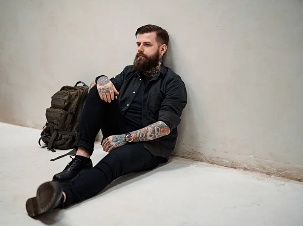 Barbudo hipster cara com mochila sentado em um chão em estúdio — Fotografia de Stock